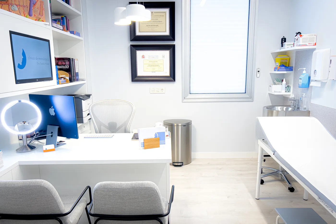 Consulta de dermatología con mesa de trabajo, camilla de exploración y diplomas en la pared