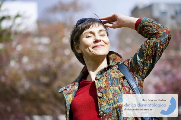Mujer con los ojos cerrados y la cara al sol en un parque con árboles en flor